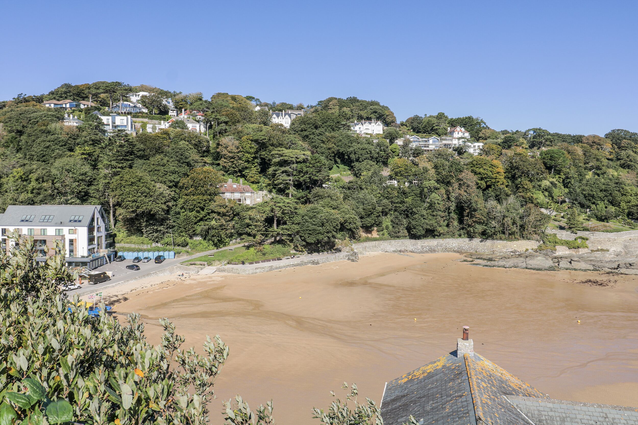 Una zona costera con casas en una ladera, una playa de arena y un litoral rocoso.