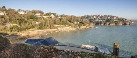 A coastal landscape with a clear view of the sea, a stone structure, and a hill with houses.