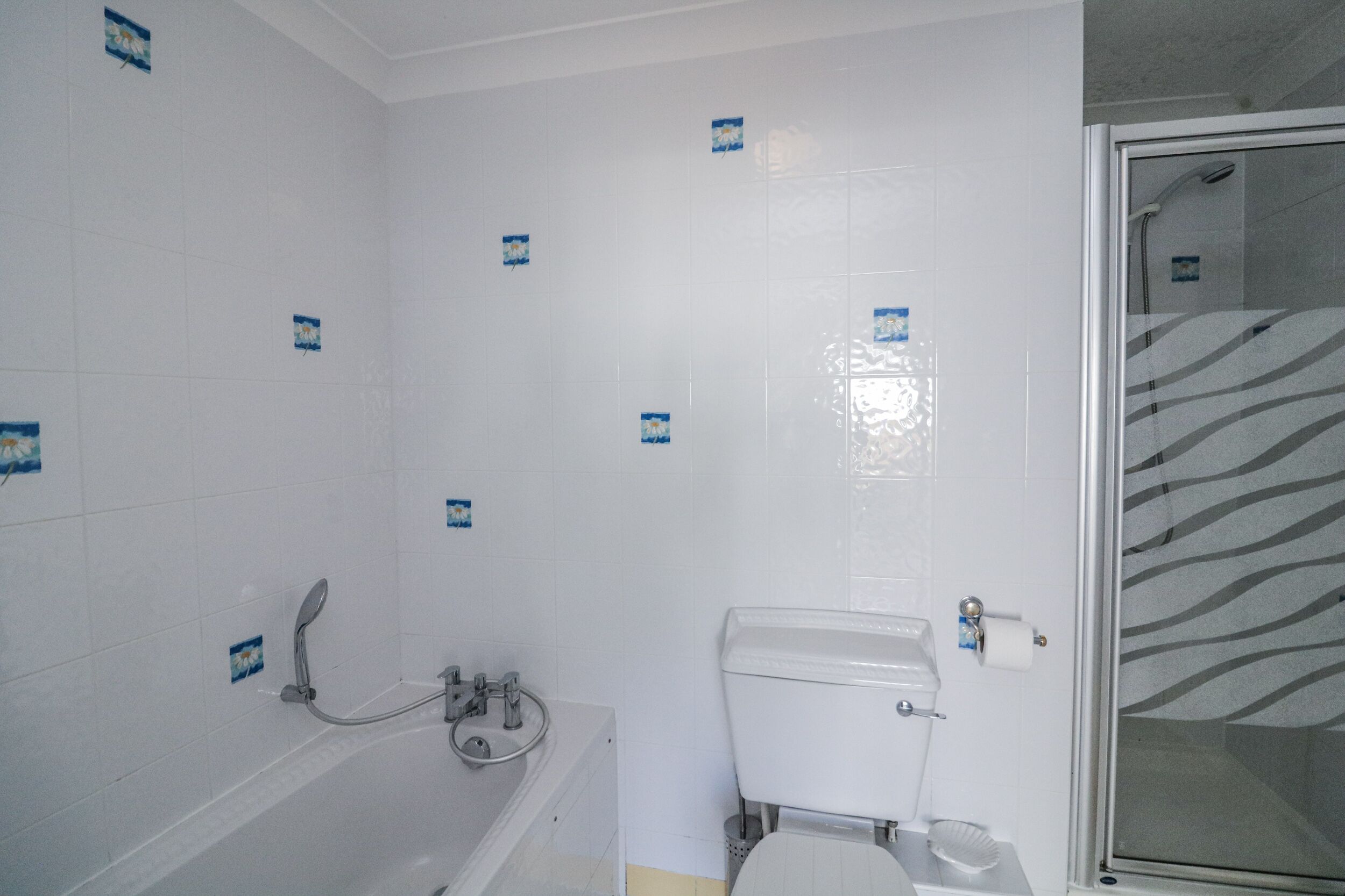 Un baño con azulejos blancos, una bañera, un inodoro y una zona de ducha.