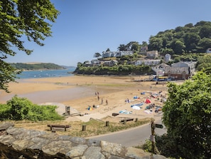 A coastal beach with a stone pathway leading to a bench, overlooking a sandy beach with umbrellas and people. - 19 Bolt Head (Salcombe)