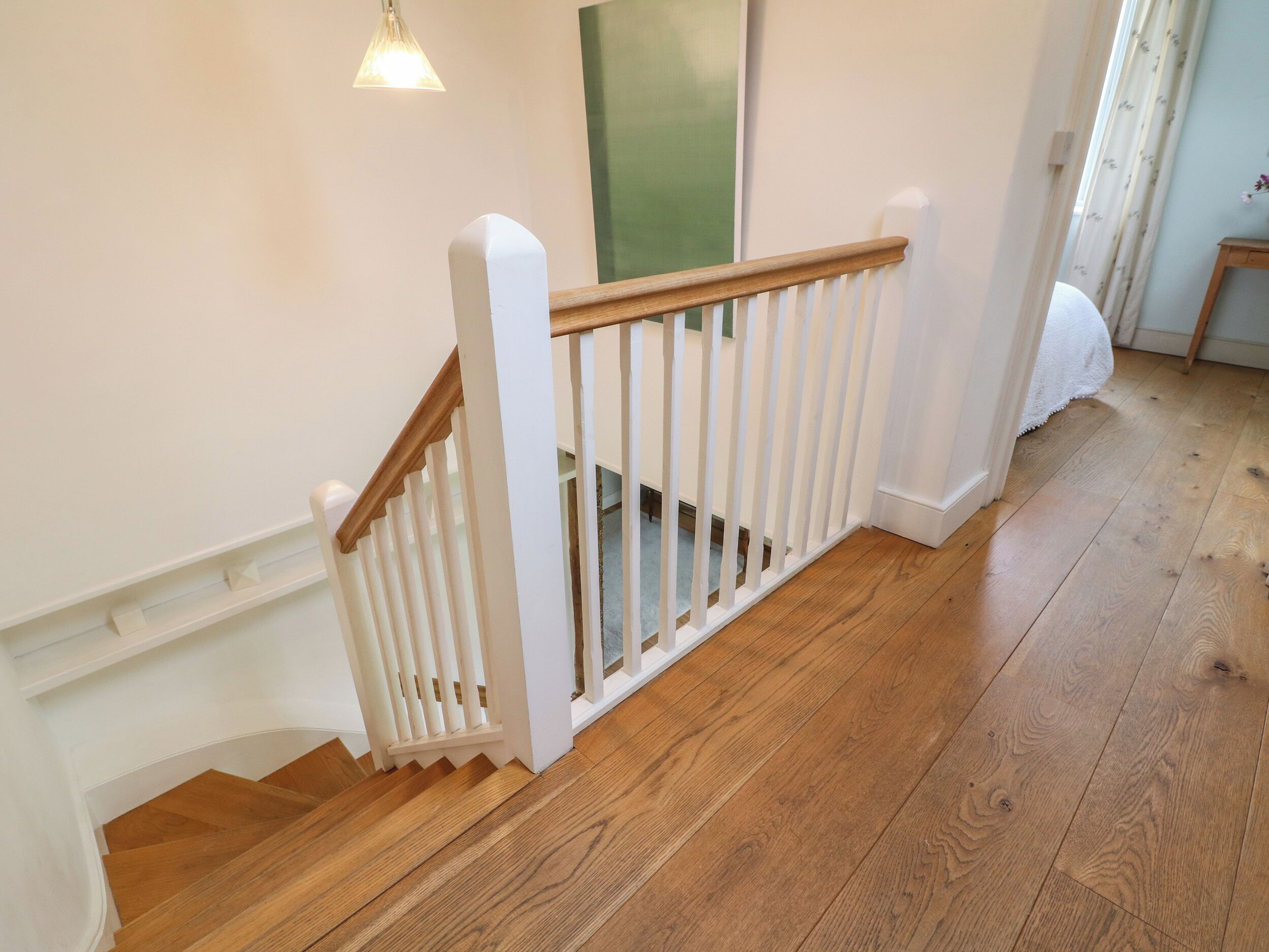 Un escalier en bois avec des rampes blanches et un luminaire au-dessus.
