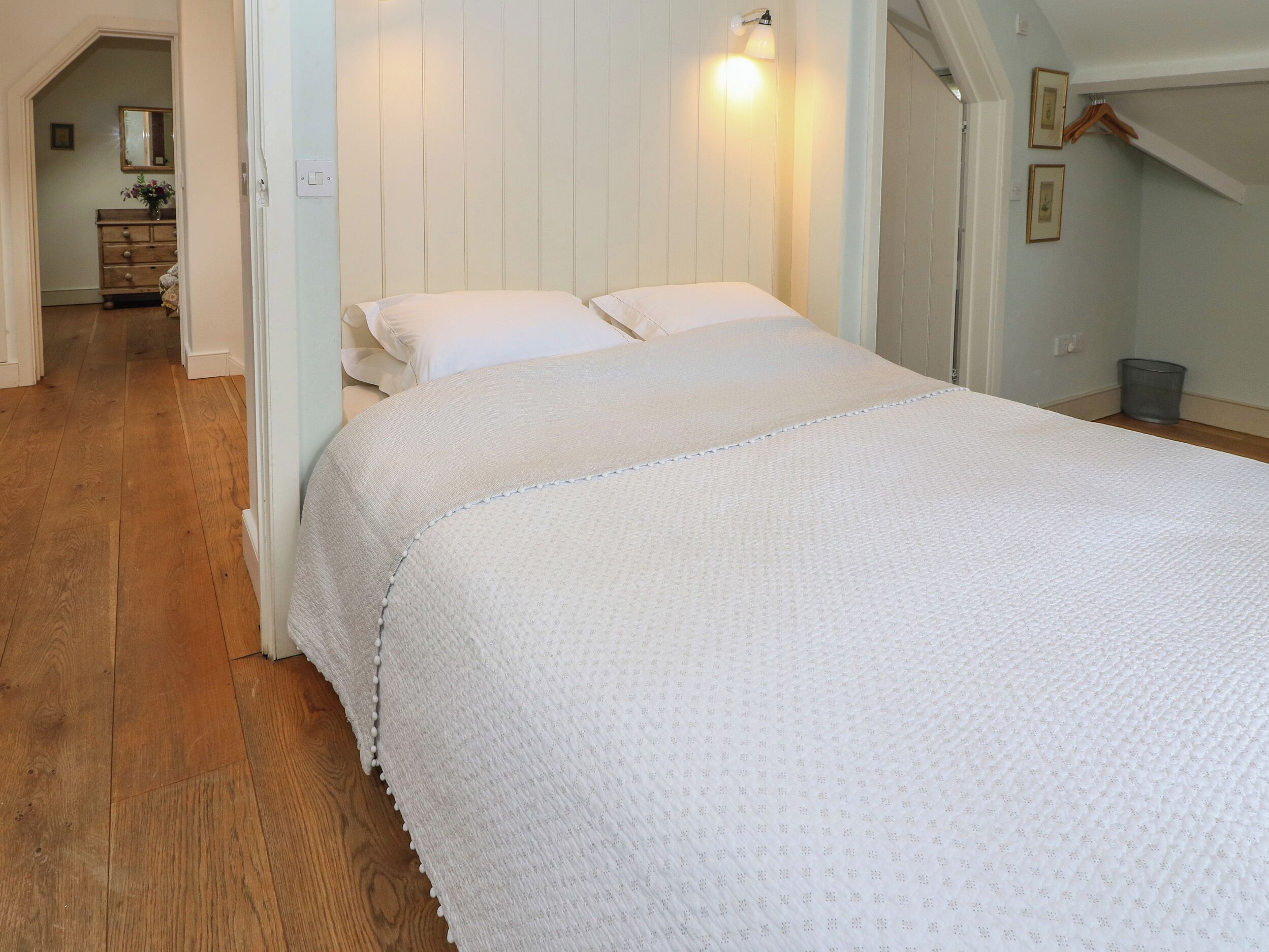 A bedroom with a large bed, wooden flooring, a dresser, and a mirror.
