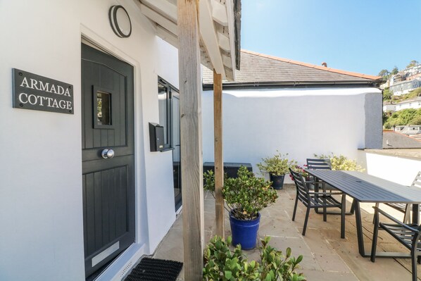 A patio area with a table and chairs, a potted plant, and a door labeled "ARMADA COTTAGE". - Armada Cottage (Dartmouth)