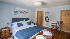 Una camera da letto con un letto, comodini in legno, una scrivania, una sedia, un quadro e una porta.