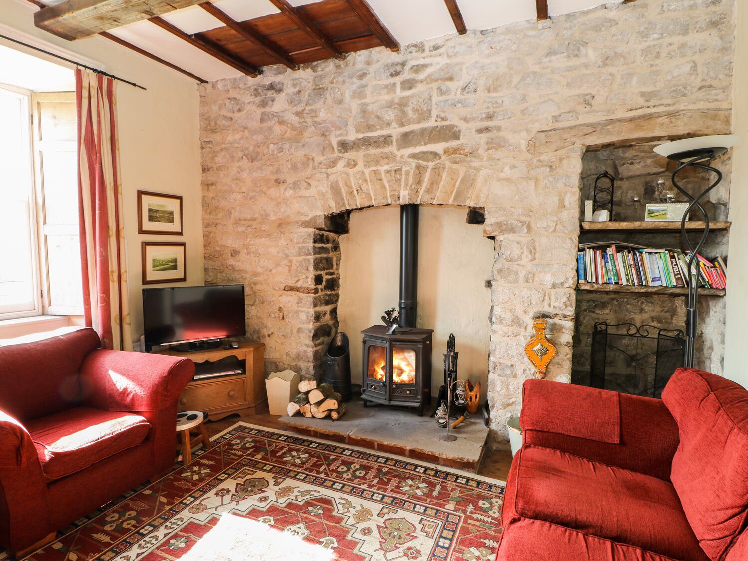 A cozy living room with a stone fireplace, a television, and two red sofas.