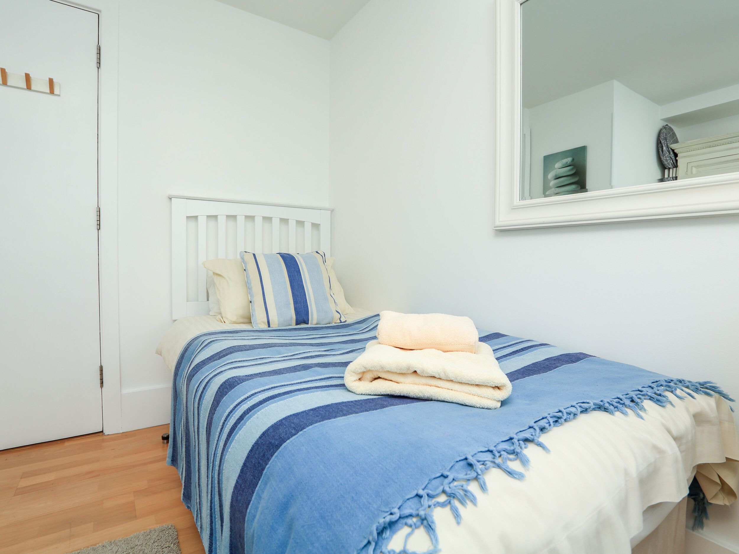 A bedroom with a bed, a white headboard, a window, and a mirror on the wall.