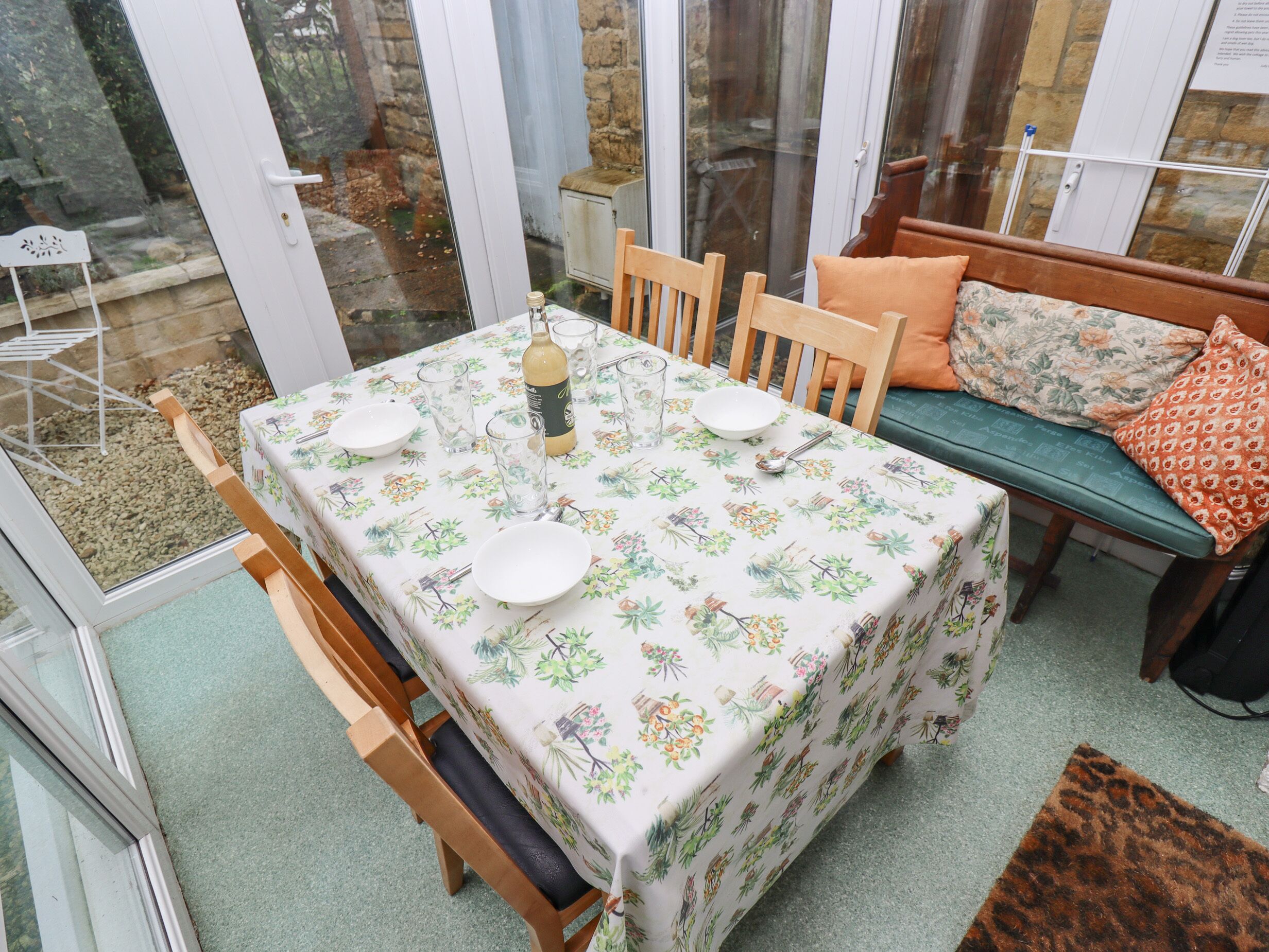 Un comedor con una mesa preparada para cuatro personas, rodeado de sillas de madera y un banco.