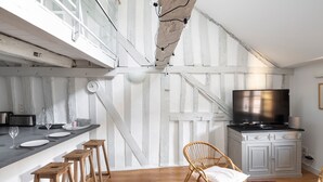 Een keuken met een houten aanrecht, krukken, een televisie en een eethoek met een stoel en tafel.