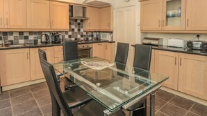 A modern kitchen with wooden cabinets, a glass dining table, and black chairs. - 5 Island Street (Salcombe)
