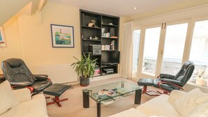 A living room with two leather chairs, a glass coffee table, a bookshelf, and a large window with curtains. - 5 Island Street (Salcombe)