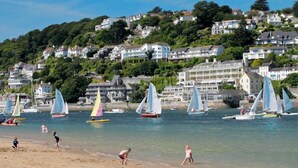 A coastal area with sailboats on the water, people on the beach, and houses on a hillside. - 5 Island Street (Salcombe)