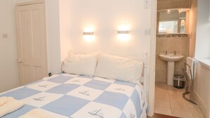 A bedroom with a bed, two bedside lamps, a door, and a bathroom with a sink and mirror. - 5 Island Street (Salcombe)