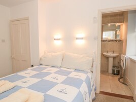 Un dormitorio con cama, dos lámparas de noche, una puerta y un baño con lavabo y espejo.