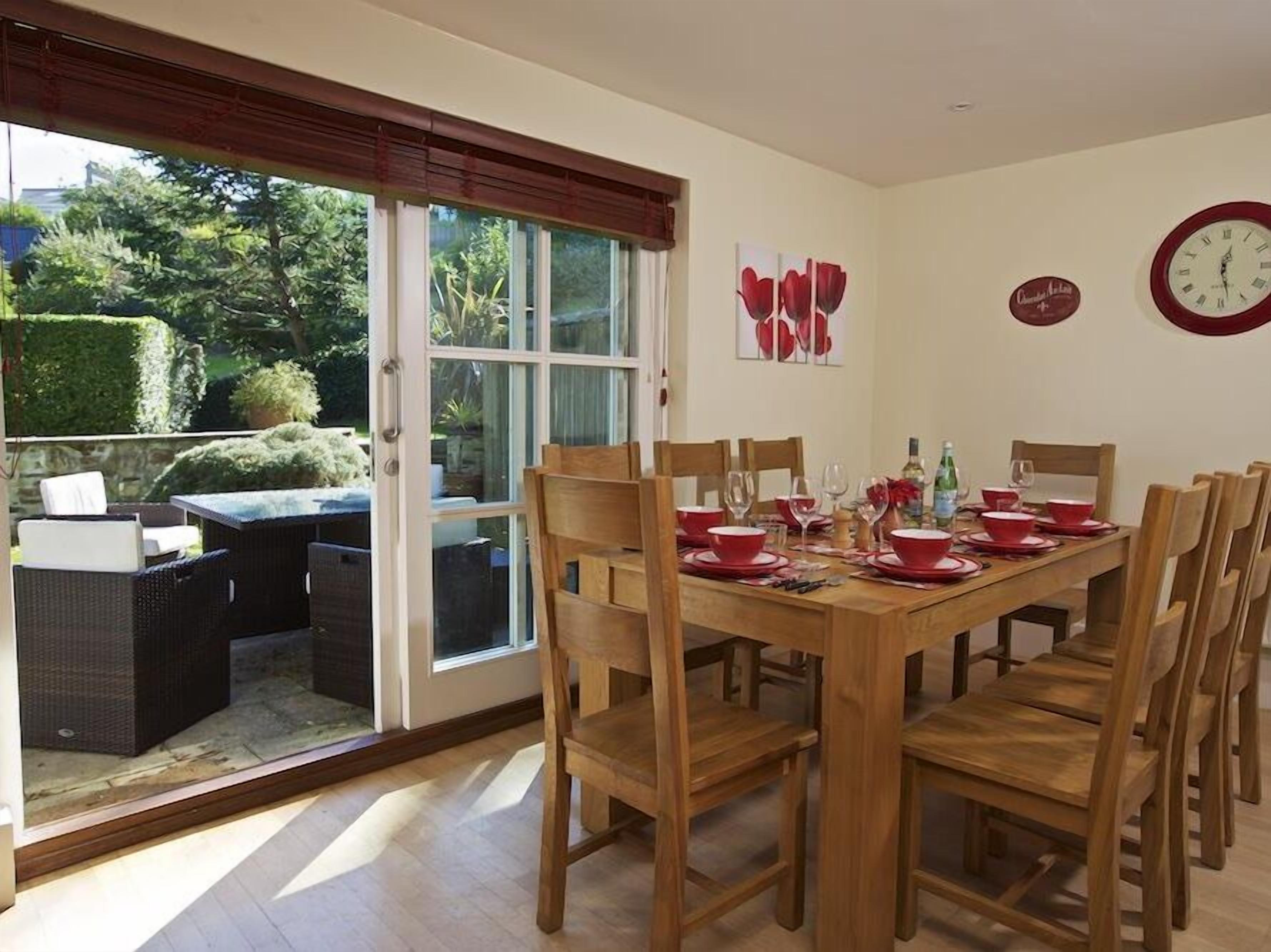 A dining area with a wooden table set for four, surrounded by wooden chairs.