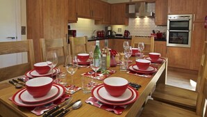 A kitchen with wooden cabinets, a double oven, and a dining table set for six with red and white plates and glasses.