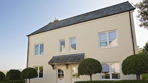 A two-story building with a flat roof, a front door, and two windows on the ground floor. There are three well-maintained hedges in front of the building.