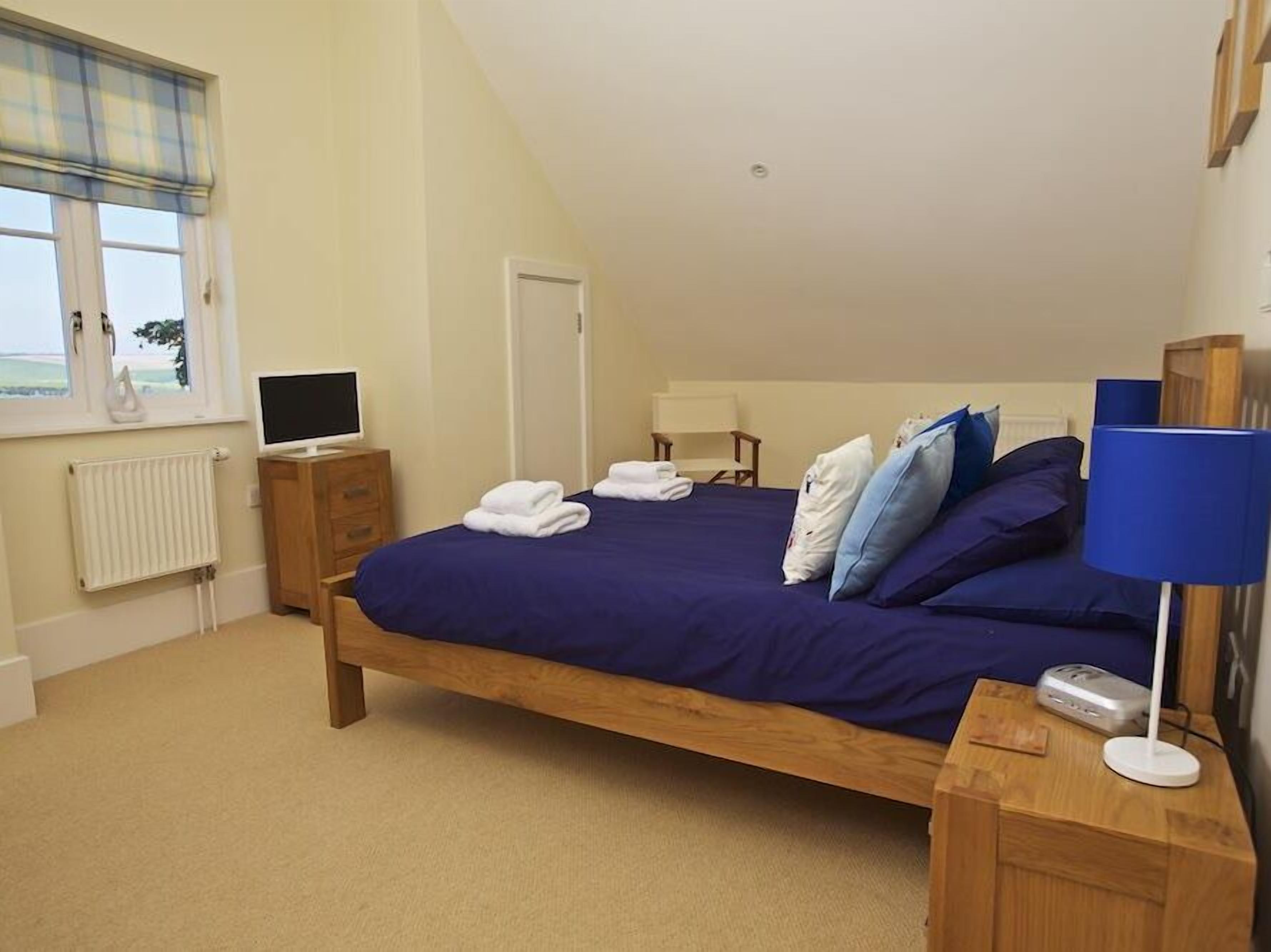 A bedroom with a bed, a bedside table, a lamp, a TV, and a window with curtains.