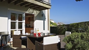 A patio with wicker furniture and a table set for dining, overlooking a residential area.