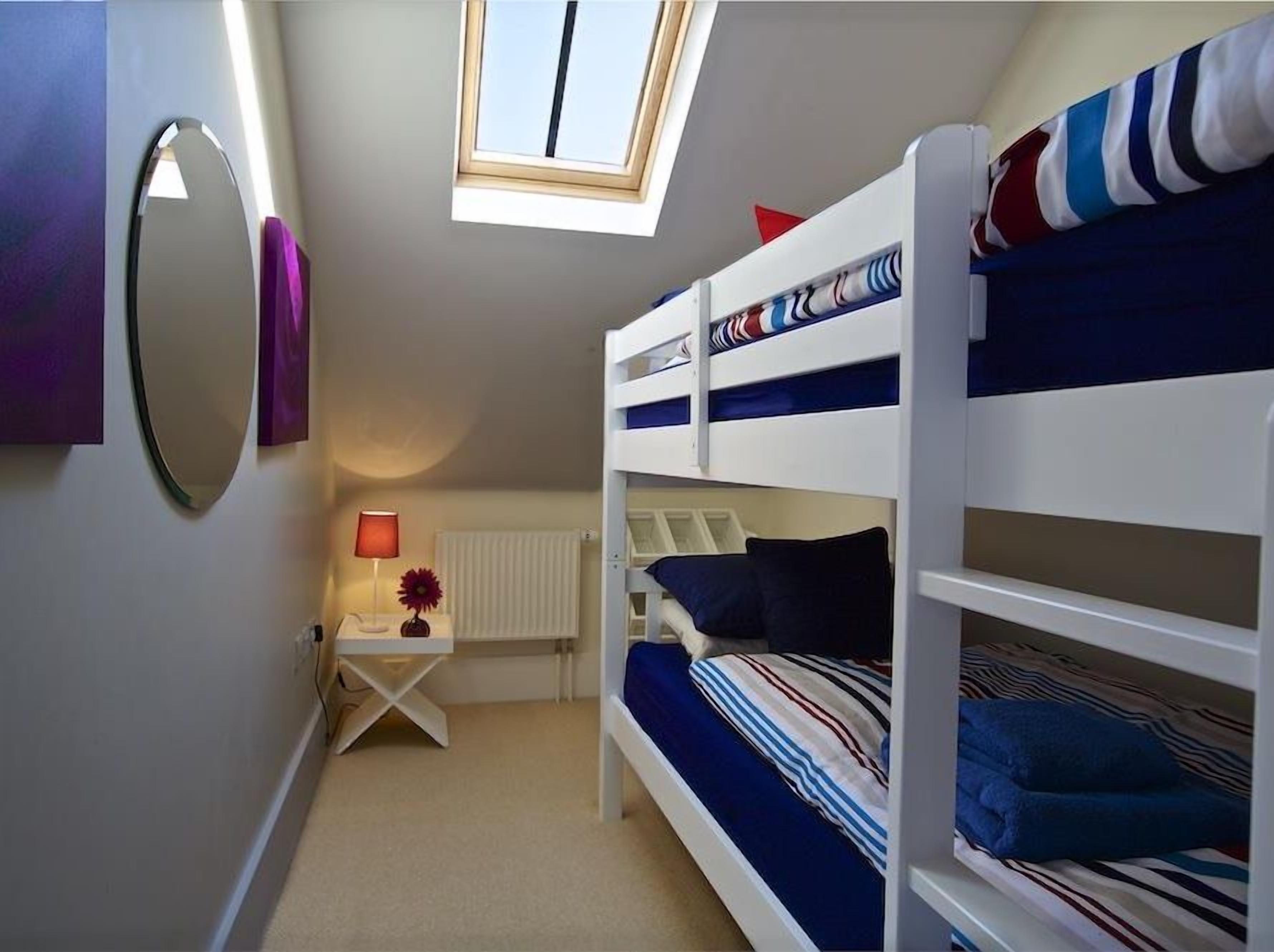 Ein kleines Zimmer mit Etagenbetten, einem kleinen Schreibtisch mit Lampe, einem Heizkörper und einem Dachfenster.