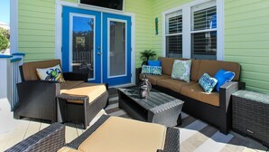 A covered outdoor patio with wicker furniture, a blue door, and a ceiling fan. - Gated 30A Home ☀️ 6 Lots from Pool | Easy Walk to Beach ☀️Outdoor Living Area w/ TV (Santa Rosa Beach)