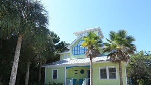 A two-story house with a front porch, a small garden, and palm trees. - Gated 30A Home ☀️ 6 Lots from Pool | Easy Walk to Beach ☀️Outdoor Living Area w/ TV (Santa Rosa Beach)