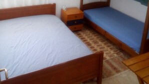 A room with a bunk bed, a single bed, a small wooden nightstand, and a patterned rug. - Ikia apartment Ierissos (Ierissos)