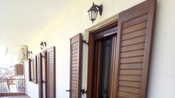 A corridor with tiled flooring, wooden shutters on the walls, and a balcony with outdoor furniture. - Ikia apartment Ierissos (Ierissos)
