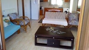 A compact living space with a sofa, two chairs, a small table, a refrigerator, a microwave, a washing machine, and a dining area with a table and chairs. - Ikia apartment Ierissos (Ierissos)