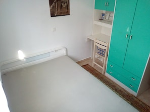 A bedroom with a bed, a wardrobe, a small table, and a shelf.