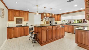 Una cocina amplia con armarios de madera, una isla grande, taburetes de bar e iluminación colgante.