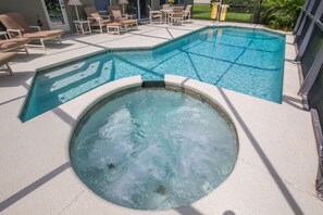 A swimming pool with a hot tub, lounge chairs, and a patio area.