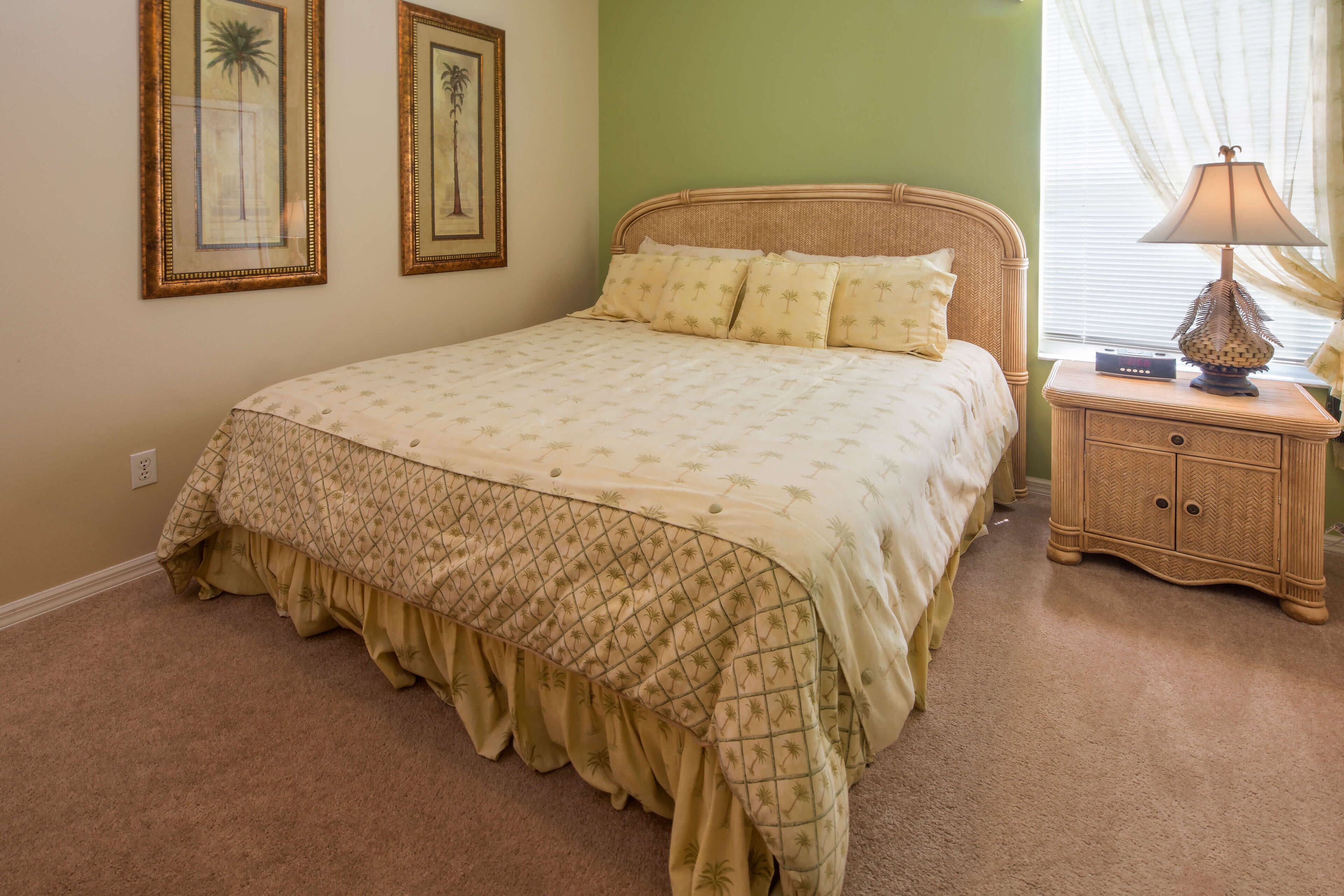 A neatly made bed with a patterned bedspread and pillows, a bedside table with a lamp, and two framed pictures on the wall.