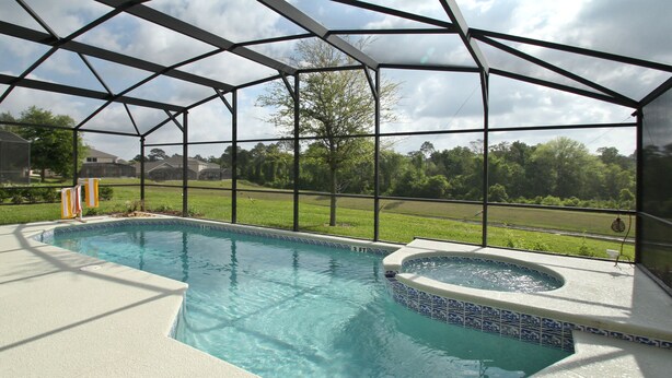 Piscina coberta com hidromassagem, rodeada por estrutura metálica e painéis de vidro, com vista para área gramada e árvores ao fundo.