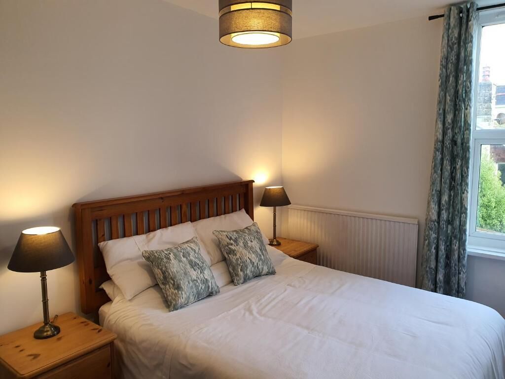 A bedroom with a wooden headboard, two bedside lamps, a bed with white bedding, and a window with curtains.