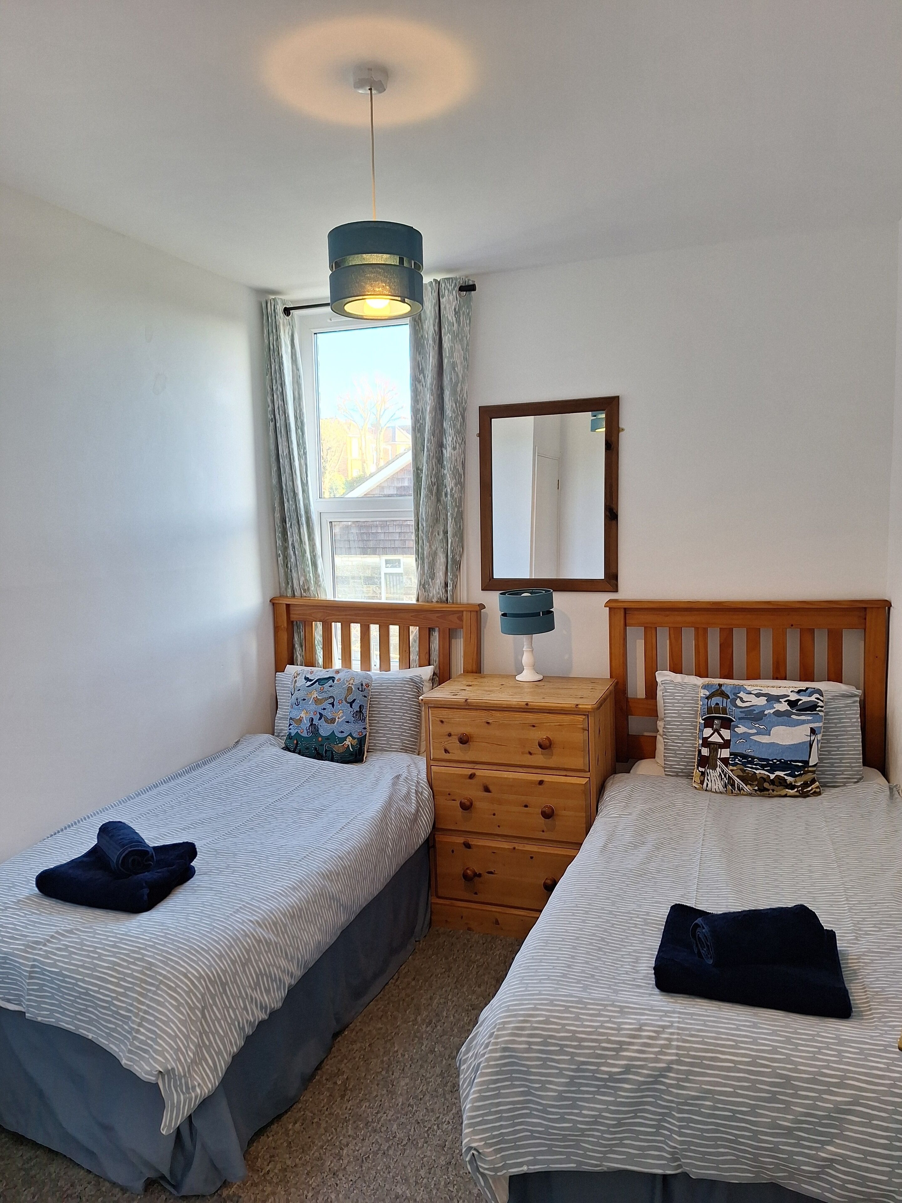 A bedroom with two single beds, a dresser, a mirror, and a window with curtains.