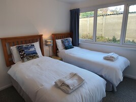 A hotel room with two single beds, each with a pillow and a folded towel. There is a nightstand with a lamp between the beds.