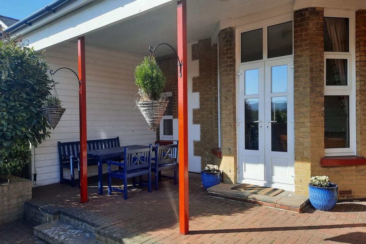 A covered patio with a table and chairs, a hanging plant, and a brick wall.