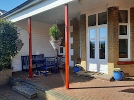 A covered patio with a table and chairs, a hanging plant, and a brick wall.
