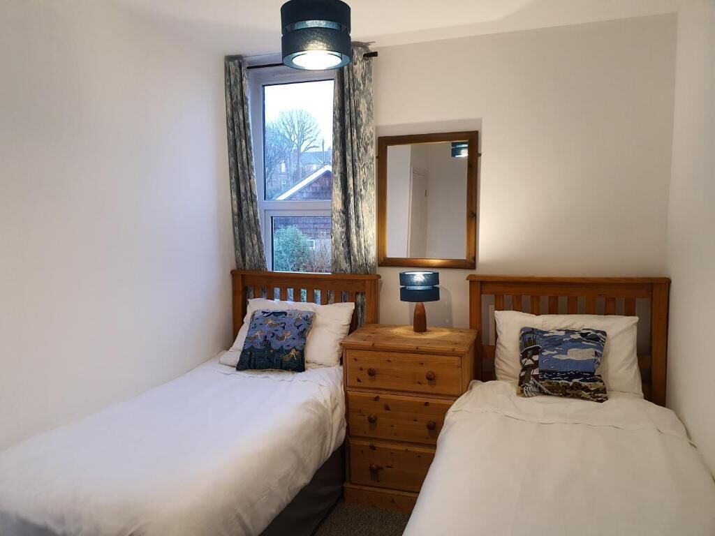 A bedroom with two single beds, a wooden dresser, a mirror, and a window with curtains.
