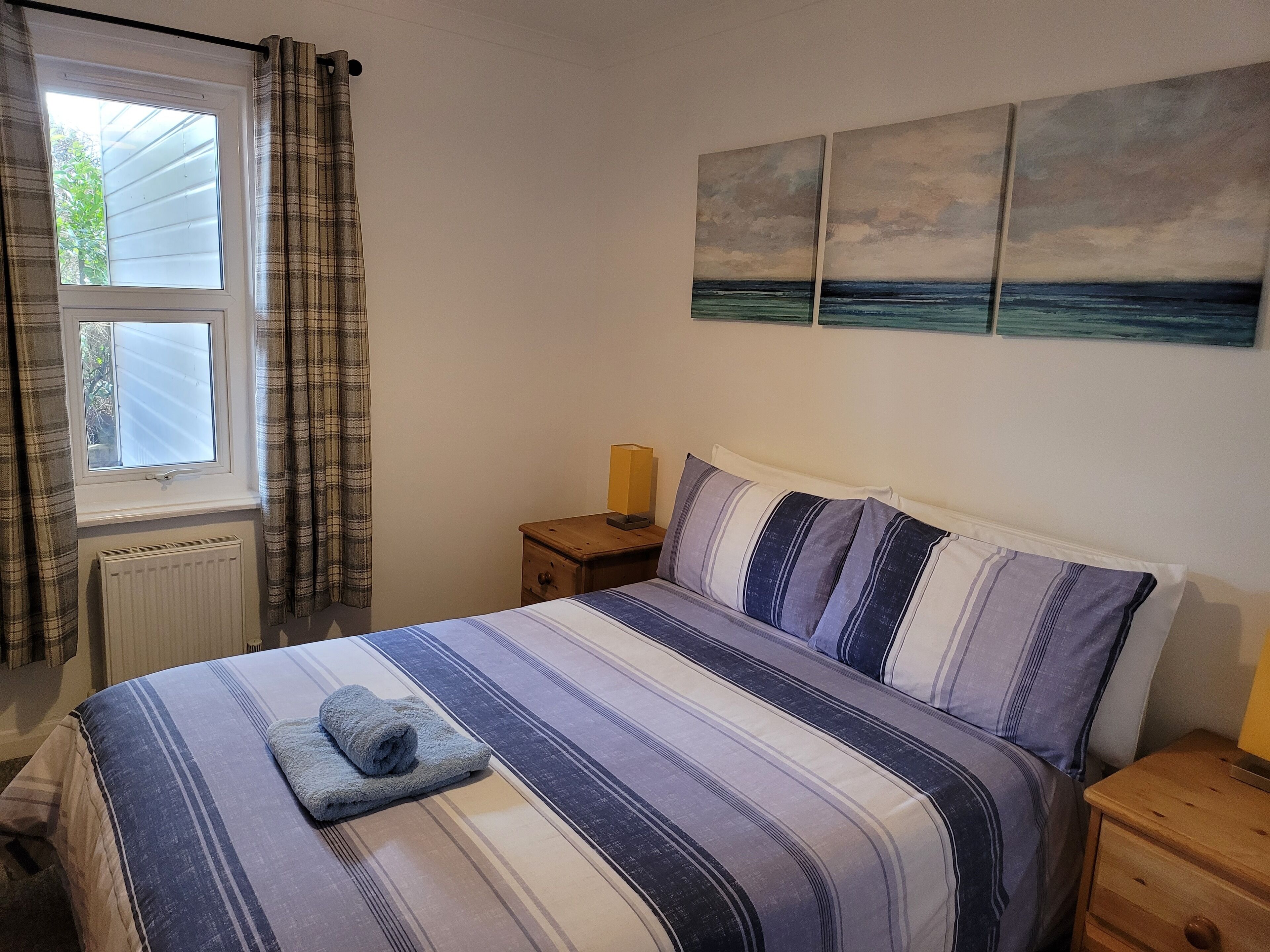 A bedroom with a bed, a nightstand, a window with curtains, and a wall with three paintings.