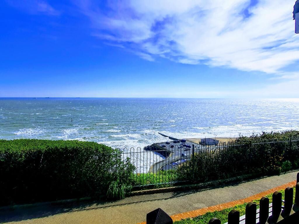 Une vue sur la côte, avec une promenade dallée, une clôture en métal et une étendue d’eau.