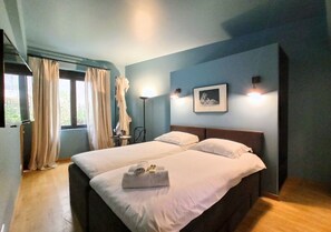 Ein Doppelbett mit weißen Bettwäsche und Handtüchern, ein Nachttisch, eine Lampe und ein gerahmtes Bild an der Wand.