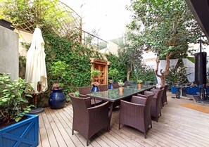 Eine Terrasse im Freien mit einem Tisch aus Glas, umgeben von Korbstühlen, Blumentöpfen und einer Pergola.