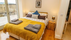 A bedroom with a bed, a wooden headboard, a nightstand, a lamp, and a view through a glass door. - Morgan's Barn (Huddersfield)