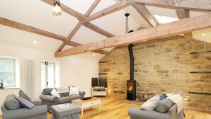 A spacious living room with a stone wall, wooden beams, a fireplace, and grey sofas. - Morgan's Barn (Huddersfield)