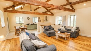 A spacious living room with wooden floors, a dining area, and a kitchen. - Morgan's Barn (Huddersfield)