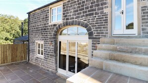 A stone building with a large arched entrance, a wooden fence, and a paved patio area. - Morgan's Barn (Huddersfield)