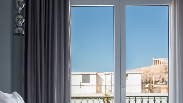 Una habitación de hotel con cama, cortinas y vista a un edificio a través de una puerta de vidrio.