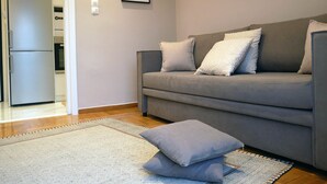 Un salón con un sofá gris, dos cojines, un tapete estampado y un cuadro en la pared.