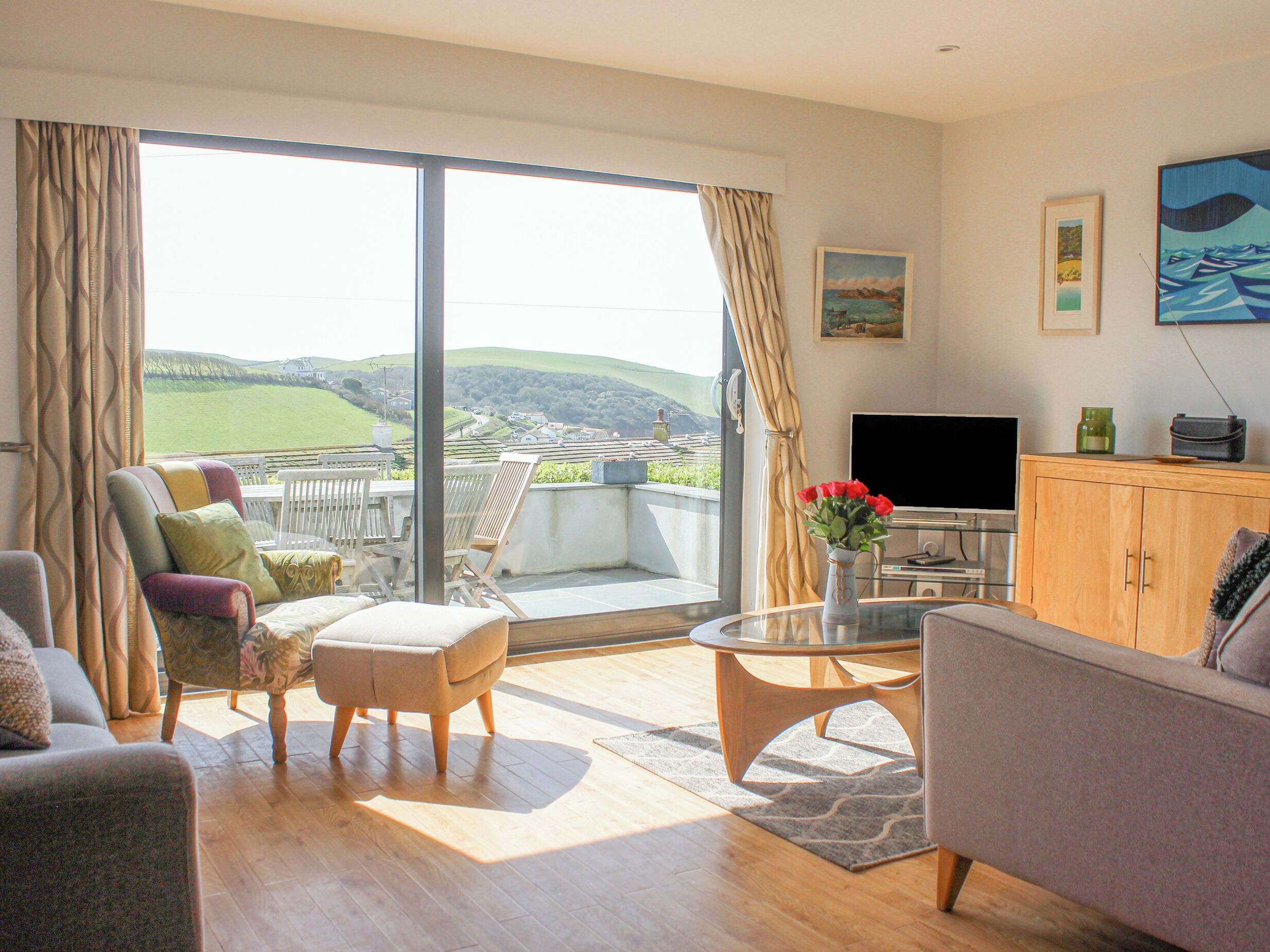 Een moderne woonkamer met een grote schuifpui naar een balkon, een flatscreen televisie en een eethoek met een tafel en stoelen.